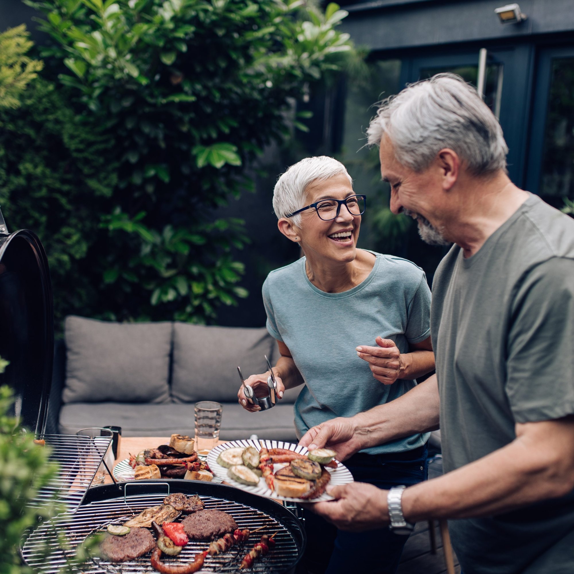 Older woman and man barbequing outside and laughing.