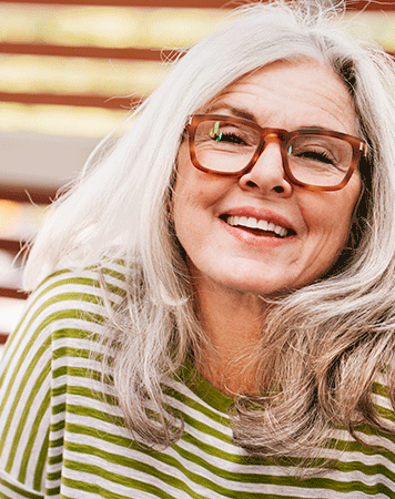 Older woman in green striped top and brown glasses smiling.